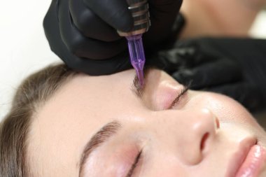 Güzellik uzmanı genç bir kadına kalıcı kaş makyajı yapıyor.