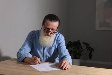 Ahşap masada son dilek ve vasiyetnameyi imzalayan kıdemli bir adam.