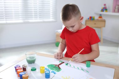 Masada fırçayla resim yapan şirin bir çocuk.