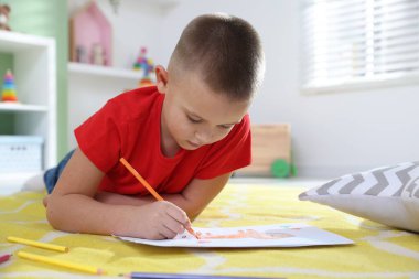 Evde yerde kalemle resim yapan şirin bir çocuk.