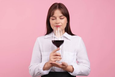 Profesyonel şarap garsonu pembe arka planda kırmızı şarap tadıyor.