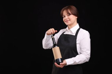 Profesyonel şarap garsonu. Siyah arka planda şarap şişesi açıyor. Mesaj için yer var.