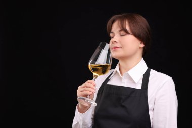 Profesyonel şarap garsonu siyah arka planda beyaz şarap tadıyor, mesaj için yer var.