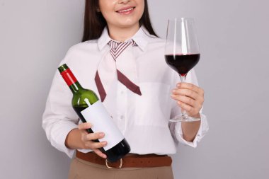 Açık gri arka planda kırmızı şarap ve şişe kadehi olan profesyonel şarap garsonu, yakın plan.