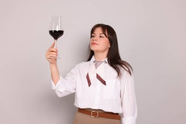 Açık gri arka planda kırmızı şarap kadehi olan profesyonel şarap garsonu.