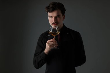 Profesyonel şarap garsonu gri arka planda beyaz şarap tadıyor.