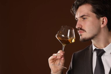 Profesyonel şarap garsonu kahverengi arka planda beyaz şarap tadıyor. Metin için boşluk