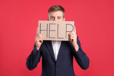 Mutsuz işadamı kırmızı arka planda kelime yazılı karton levha tutuyor.