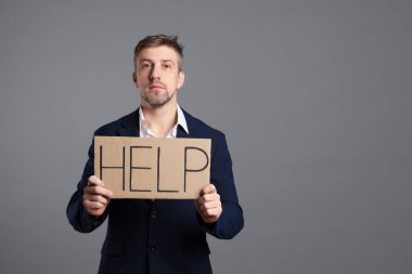 Mutsuz işadamı kelime ile karton işareti tutuyor Gri arkaplanda yardım, metin için boşluk