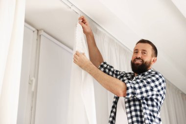 Evde pencere perdelerini asan adam, düşük açılı görüntü.