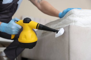 Haşere kontrol işçisi yatağı temizliyor, kapalı alanda buhar temizleyicisiyle, yakın plan