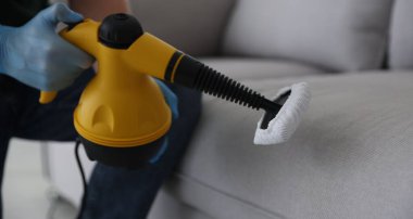 Haşere kontrol işçisi kanepeyi temizliyor. Kapalı alanda buhar temizleyicisi var.