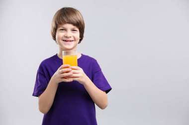 Açık gri arka planda bir bardak taze portakal suyu olan çocuk. Metin için boşluk