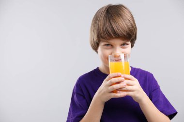 Açık gri arka planda bir bardak taze portakal suyu olan çocuk. Metin için boşluk