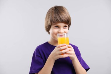Açık gri arka planda bir bardak taze portakal suyu olan çocuk.