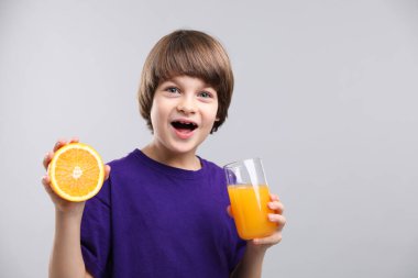 Açık gri arka planda bir bardak taze portakal suyu ve meyveli çocuk. Metin için boşluk