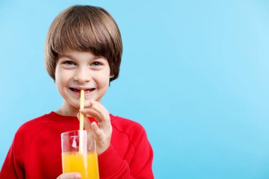 Açık mavi arka planda bir bardak taze portakal suyu olan çocuk. Metin için boşluk