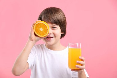 Pembe arka planda bir bardak taze portakal suyu ve meyveli çocuk.