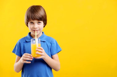 Sarı arka planda bir bardak taze portakal suyu olan çocuk. Metin için boşluk