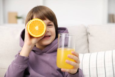 Evdeki kanepede bir bardak taze portakal suyu olan çocuk. Metin için boşluk