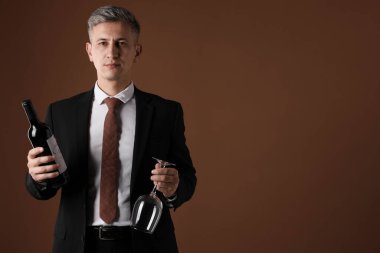 Kahverengi arka planda kırmızı şarap ve cam şişesi olan profesyonel şarap garsonu.