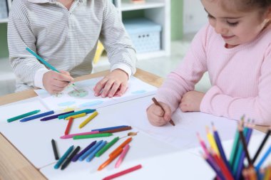Çocuklar kalem ve pastel boyayla resim çiziyor.