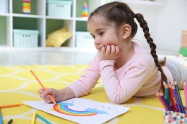 Evde yerde kalemle çizen sevimli küçük kız.