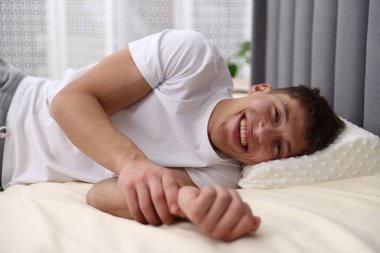 Evde ortopedik yastıkla yatakta yatan gülümseyen adam. Sağlıklı duruş