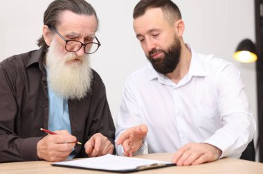 Noter, kıdemli adama ofisteki ahşap masada son arzusunu ve vasiyetnamesini imzalayacağı yeri gösteriyor.