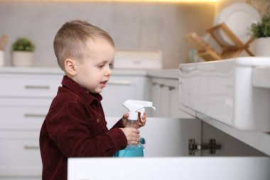 Evde çocuk güvenliği. Mutfakta bir şişe temizlik malzemesi olan küçük çocuk, mesaj için yer var.