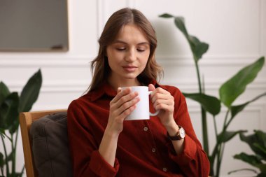 Evdeki koltukta bir fincan aromatik kahveli kadın.