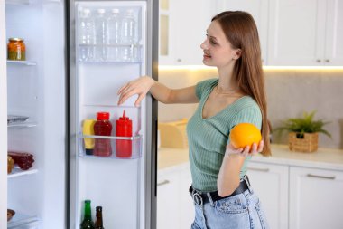 Mutfakta portakallı kadın açık buzdolabının yanında.