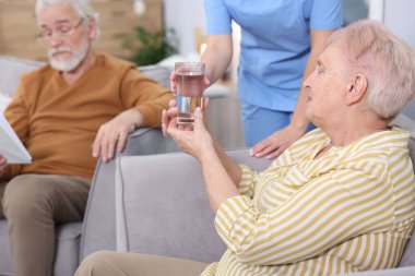 Huzurevindeki yaşlı kadına bir bardak su veren bakım görevlisi, yakın plan.