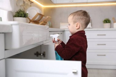Evde çocuk güvenliği. Mutfakta bir şişe temizlik malzemesi olan küçük bir çocuk.