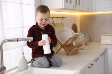 Evde çocuk güvenliği. Küçük çocuk mutfakta lavabonun yanında tozla oynuyor, mesaj için yer var.