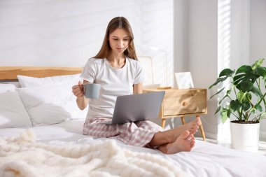 Elinde kahve olan bir kadın evde dizüstü bilgisayarla çalışıyor.