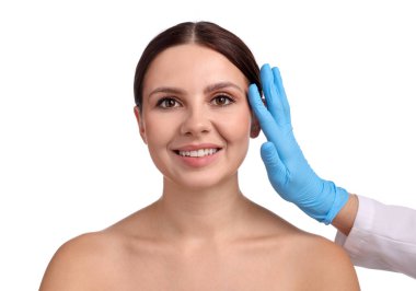 Doktor, estetik ameliyattan önce beyaz arka planda hastanın yüzünü kontrol ediyor.