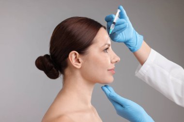 Estetik ameliyat. Doktor gri arka plandaki hastaya yüz enjeksiyonu yapıyor.