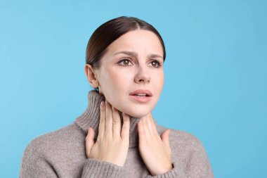 Açık mavi arka planda boğaz ağrısı çeken bir kadın. Soğuk Semptom