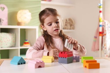 Küçük kız oyun odasındaki beyaz masada oyuncaklarla oynuyor.