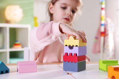 Oyun odasındaki beyaz masada oyuncaklarla oynayan mutlu küçük kız, seçici odaklanma