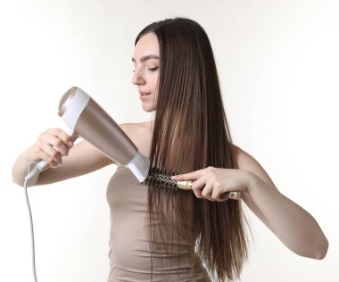 Saçını saç kurutma makinesiyle şekillendiren ve beyaz arka planda tarayan güzel bir kadın.