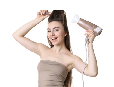 Saçını saç kurutma makinesiyle şekillendiren ve beyaz arka planda tarayan mutlu bir kadın.