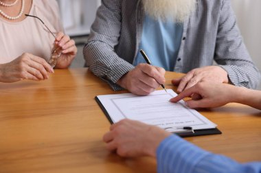 Noter, ahşap masada son arzuları ve vasiyetnameleri imzalayacakları yeri gösteriyor.