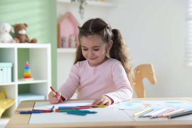 Masada pastel boyayla resim çizen sevimli küçük kız.