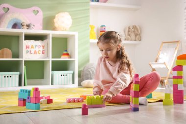 Küçük kız oyun odasında yerde oyuncaklarla oynuyor.