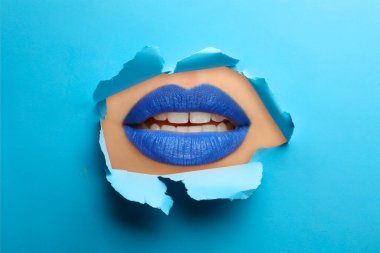Güzel dolgun dudaklı kadın, mavi kağıttaki yırtık delikten bakıyor.