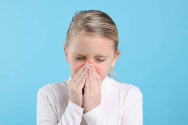 Açık mavi arka planda hapşıran küçük bir kız. Soğuktan muzdarip.