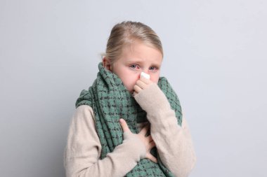 Gri arka planda soğuk algınlığından muzdarip dokusu ve atkısı olan küçük bir kız. Kırmızı gözler ve burun.