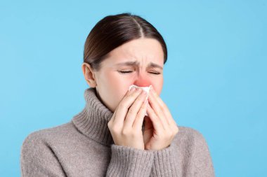Açık mavi arka planda hapşıran dokuları olan hasta bir kadın. Soğuktan acı çekiyor. Kırmızı burun.